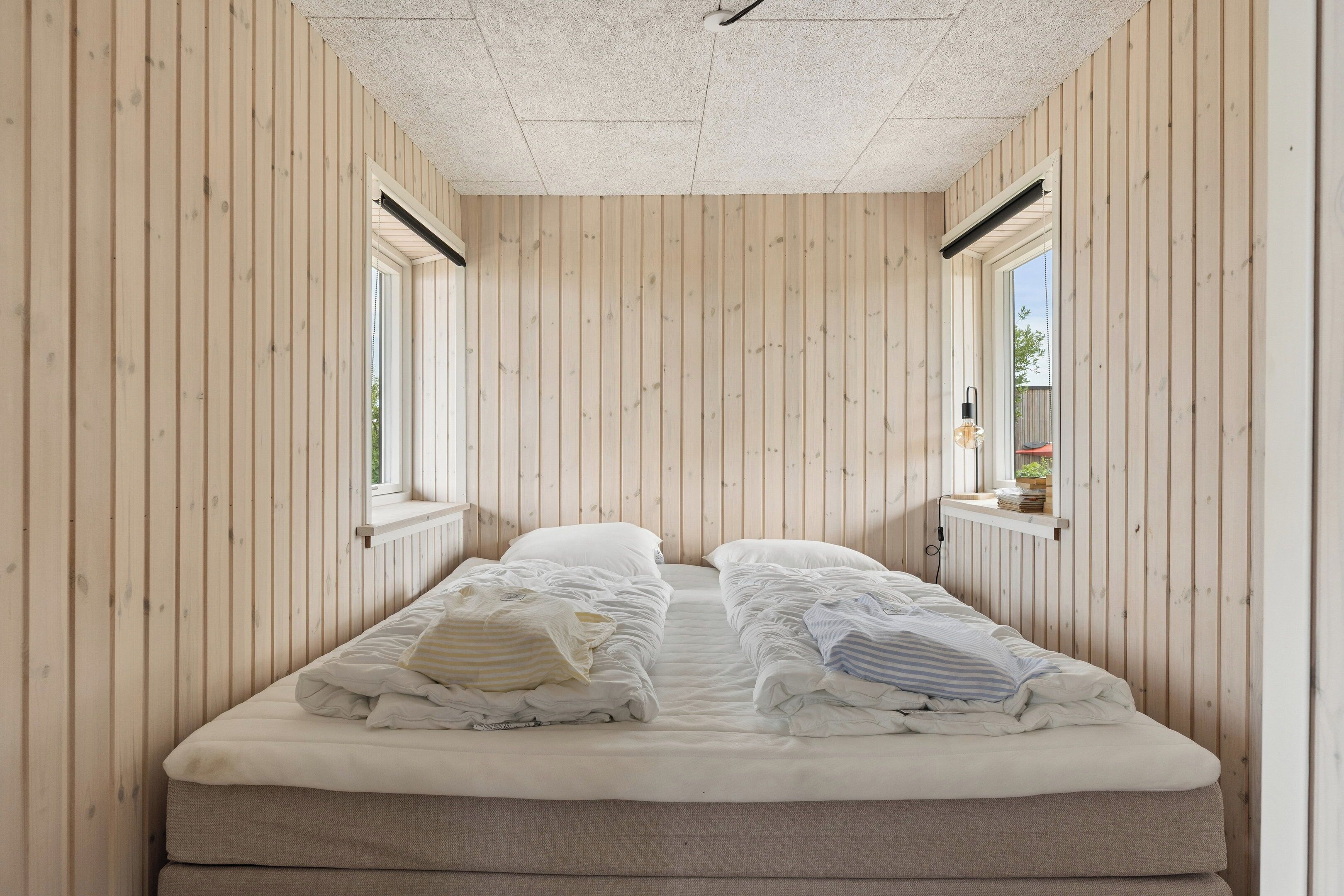 Een kleine kamer met een bed, houten wanden en een raam.