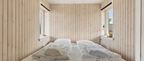 Een kleine kamer met een bed, houten wanden en een raam.