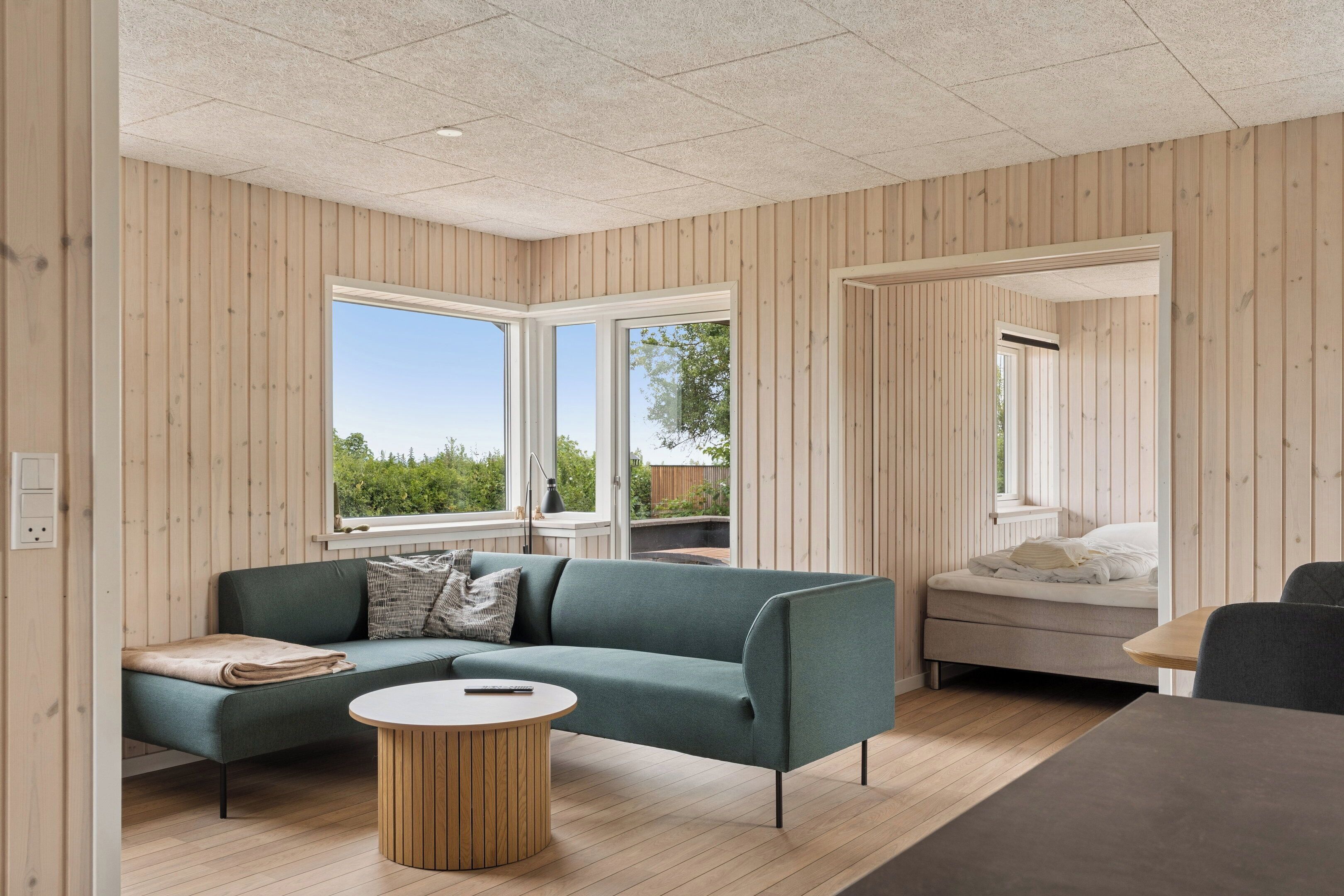 A modern interior with a sofa, a round table, a bed, and large windows.