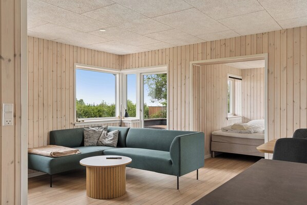 A modern interior with a sofa, a round table, a bed, and large windows. - Renovated beach house with unique location (Bjert)