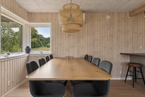 Een vergaderruimte met een lange houten tafel, donkere stoelen, een geweven hanglamp en een raam met uitzicht op groen.