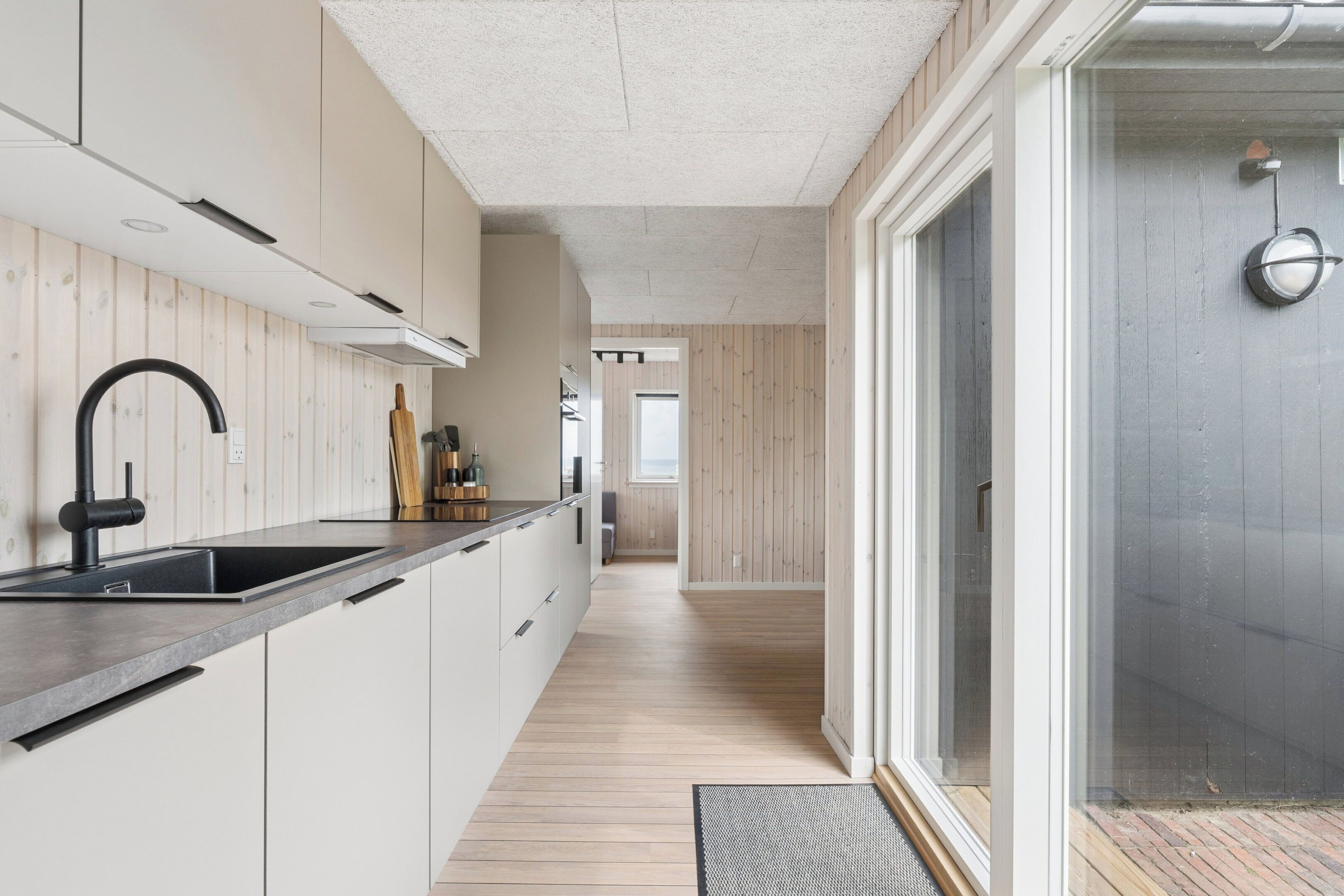 A modern kitchen with a black faucet, wooden flooring, and a view of the outside.