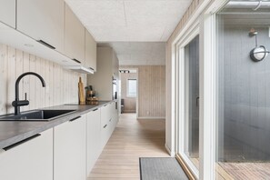 A modern kitchen with a black faucet, wooden flooring, and a view of the outside. - Renovated beach house with unique location (Bjert)