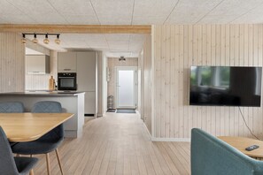 A modern kitchen with a built-in oven and a dining area with a wooden table and chairs. - Renovated beach house with unique location (Bjert)