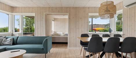A modern interior with a sofa, dining table, and chairs, wooden floors, and large windows.