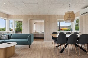 Een modern interieur met een bank, eettafel, stoelen, houten vloeren en grote ramen.