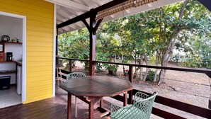 A covered outdoor area with a wooden table and chairs, a hanging light fixture, and a view of greenery. - Beach bungalow: Frégate (Le Carbet)