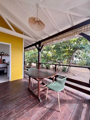 Un espacio exterior techado con una mesa y sillas de madera, una lámpara colgante y vistas al follaje.