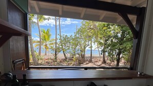 A kitchen with a window view of a beach, a sink, and various kitchen items. - Beachfront Bungalow: Pelican (Le Carbet)