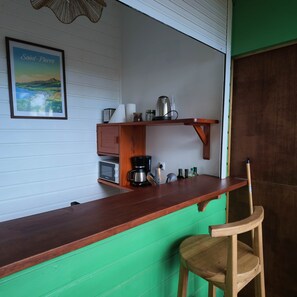 A kitchen area with a wooden countertop, a coffee maker, a microwave, and a shelf with kitchen items.