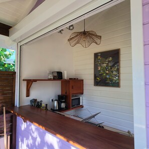 Une cuisine avec un plan de travail en bois, un luminaire suspendu, un tableau noir servant de menu et un petit réfrigérateur.