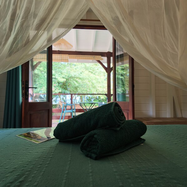 A room with a bed, a window, and a view of greenery outside. - Beach Bungalow: Thazard (Le Carbet)
