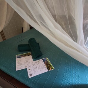 A bed with a teal bedspread, a rolled-up towel, and printed materials including a welcome card and a service information sheet. - Beach bungalow: Thazard (Le Carbet)
