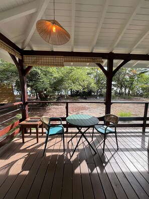 Un espace extérieur abrité, doté d’une table et de chaises, d’un luminaire suspendu, et offrant une vue sur des arbres et une clôture.
