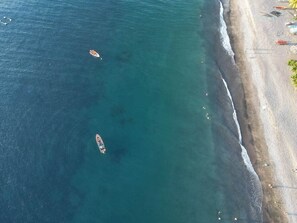 Vista aérea de una playa con aguas cristalinas y algunas embarcaciones.