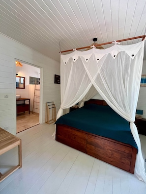 Une chambre à coucher avec un lit en bois, des murs blancs, un plafond en bois et un lit à baldaquin blanc.