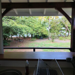 A view from inside a building looking out to a garden with trees and a barbecue area. - Beach bungalow: Thazard (Le Carbet)