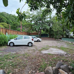 Un área de estacionamiento con dos autos, rodeada de follaje y una valla de madera.