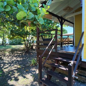 A wooden deck with a staircase leading to a covered area, surrounded by greenery and trees.