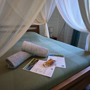 Una cama con una colcha verde, una toalla enrollada y un folleto de bienvenida.