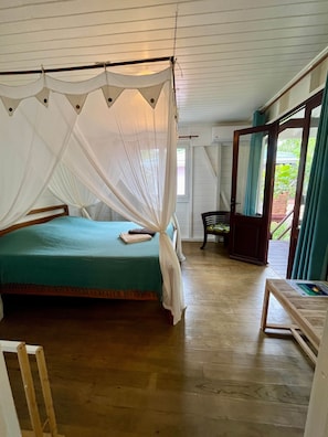 Ein Zimmer mit einem Bett, einem Holzstuhl, einem Tisch mit einem Buch und einem Fenster mit Vorhängen.