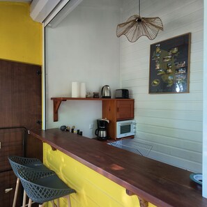 A kitchen with a wooden countertop, a hanging light fixture, a coffee maker, a toaster, and a framed menu on the wall.