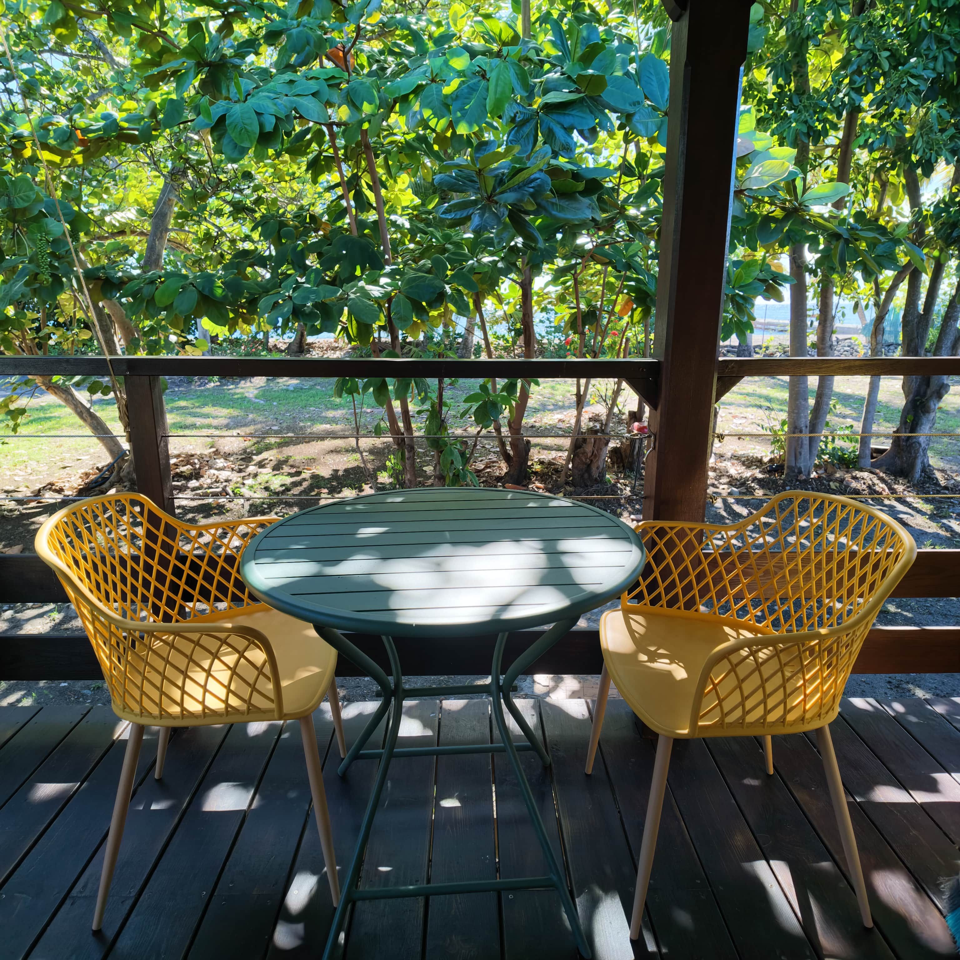 Eine Holzterrasse mit zwei gelben Stühlen und einem Tisch, umgeben von Grünpflanzen und Bäumen.