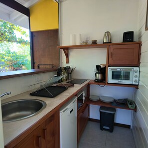 A compact kitchen with a sink, a microwave, a coffee maker, and a small trash bin.