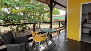 A covered outdoor seating area with dark wooden flooring, wicker chairs, and a hanging light fixture. - Beach bungalow: Balaou (Le Carbet)