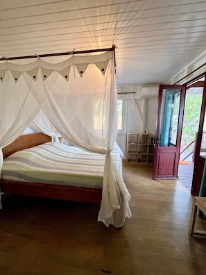 Una habitación con cama con dosel, suelo de madera, una pequeña mesa y una puerta que da al exterior.