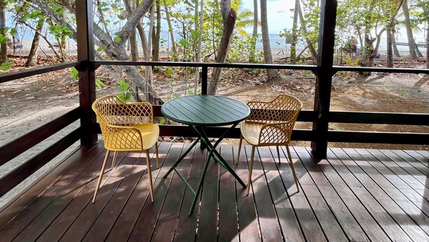 A covered outdoor area with a wooden deck, a table with chairs, and a hanging light fixture. - Beach bungalow: Barracuda (Le Carbet)