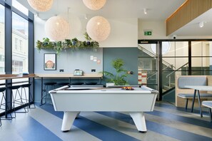 A pool table in a modern lounge area with bar stools, a counter, and a staircase leading to an upper level. - Student Only St Teresa House (Plymouth)