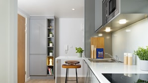A modern kitchen with a built-in microwave, a sink, and a wooden bar stool. - For Students Only Studios in Plymouth (Plymouth)
