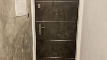 Ein Korridor mit einer dunkelholzigen Tür, einer weißen Wand und einem strukturierten Boden.