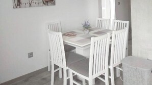 Un comedor con una mesa y sillas blancas, una planta en maceta y un cuadro en la pared.