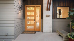 A wooden front door with a glass panel, a mailbox, and a stone bench outside a house with a sloped roof and wooden beams. - Bellingham Adventure Home: 4BR Retreat w/ Yard Near Trails (Bellingham)