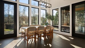 A dining area with a table and chairs, large windows, and a hanging light fixture. - Bellingham Adventure Home: 4BR Retreat w/ Yard Near Trails (Bellingham)