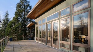 A modern building with large glass doors and windows, a covered patio area, and a view of surrounding trees. - Bellingham Adventure Home: 4BR Retreat w/ Yard Near Trails (Bellingham)