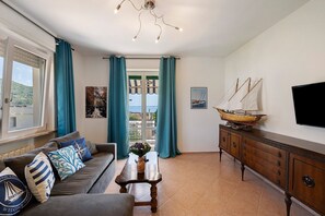 Una sala de estar con sofá, mesa de centro, televisor, aparador y vistas a través de una puerta.