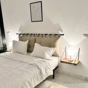 A bedroom with a bed, pillows, a bedside table with a lamp, a framed picture on the wall, and a window with curtains. - La Casa Verde , Duplex in the Heart of La Marsa (La Marsa)