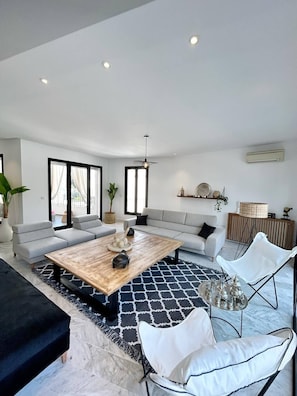 A modern living room with a large sofa, a coffee table, and a white armchair. There are potted plants and a hanging light fixture. - La Casa Verde , Duplex in the Heart of La Marsa (La Marsa)