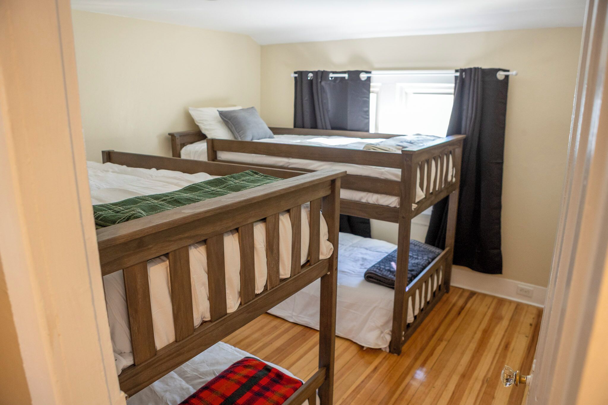 A room with bunk beds, a window with curtains, and wooden flooring.