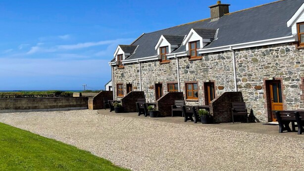 A stone building with multiple windows and doors, a gravel driveway, and outdoor seating. - Tuskar Holiday Cottage, Mill Road Farm (Kilmore Quay)