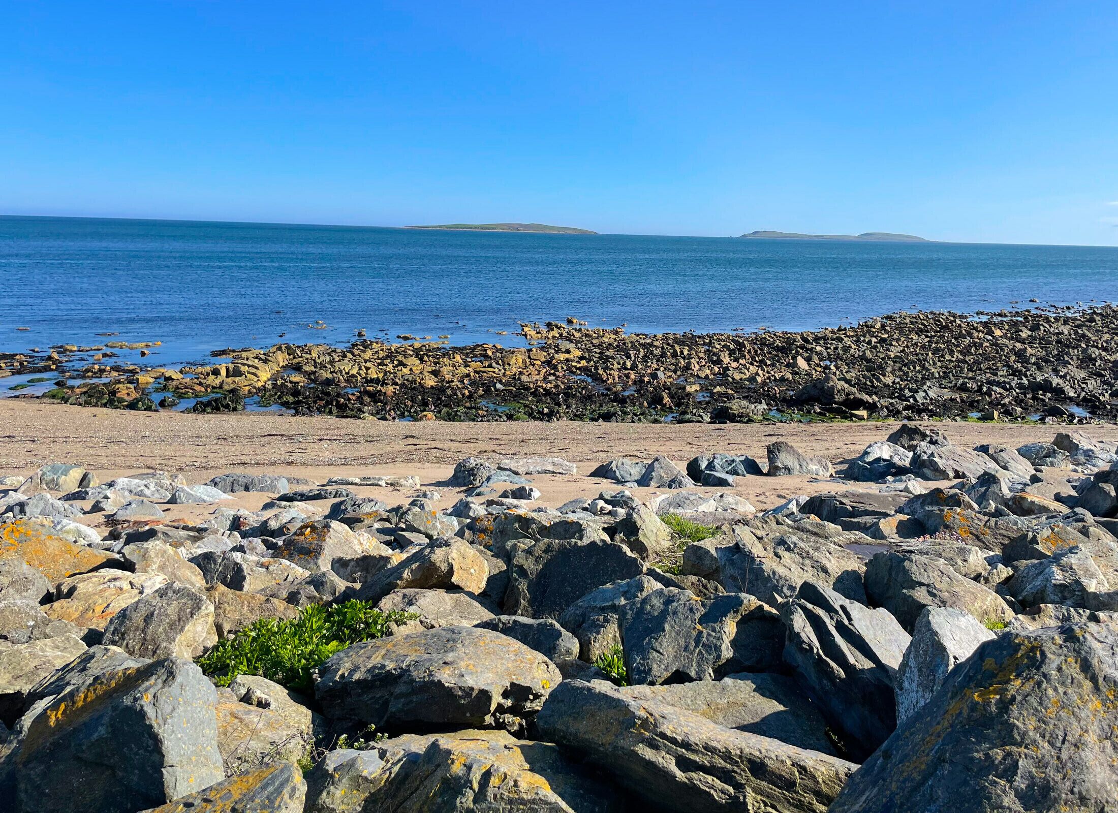 A rocky beach with large boulders and a view of the sea and distant land.