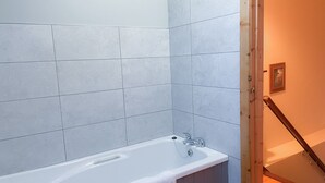 A bathroom with a white bathtub, tiled walls, and a wooden staircase. - Tuskar Holiday Cottage, Mill Road Farm (Kilmore Quay)