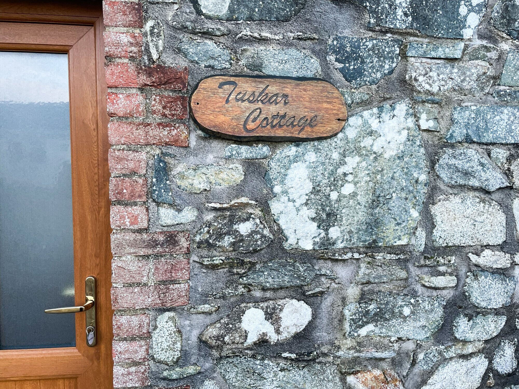 Eine rustikale Steinmauer mit einem Holzschild, auf dem 'Tasher Cottage' steht.