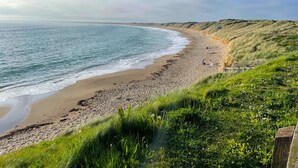 A beach with a curved shoreline, grassy dunes, and a clear sky. - Tuskar Holiday Cottage, Mill Road Farm (Kilmore Quay)