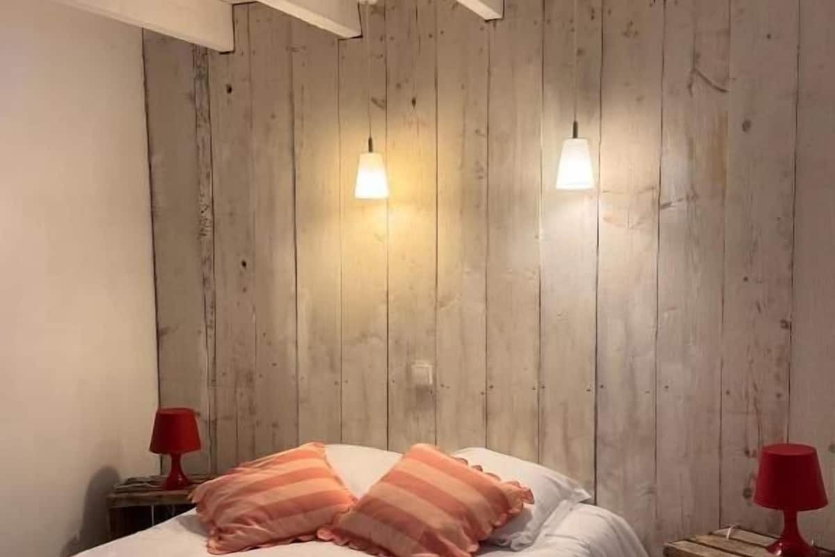 Ein Schlafzimmer mit einer Holzwand, einem Bett mit weißer Bettwäsche, zwei roten Lampen auf Nachttischen und einem kleinen Holzschrank.