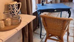 A cozy room with a wicker chair, a small table with a mug and jars, and a blue table in the background. - Motel - Usine à Gaz (Bourgueil)