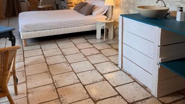 A bedroom with a stone wall, a bed, a bedside table with a lamp, a dresser, and a window with curtains. - Motel - Usine à Gaz (Bourgueil)